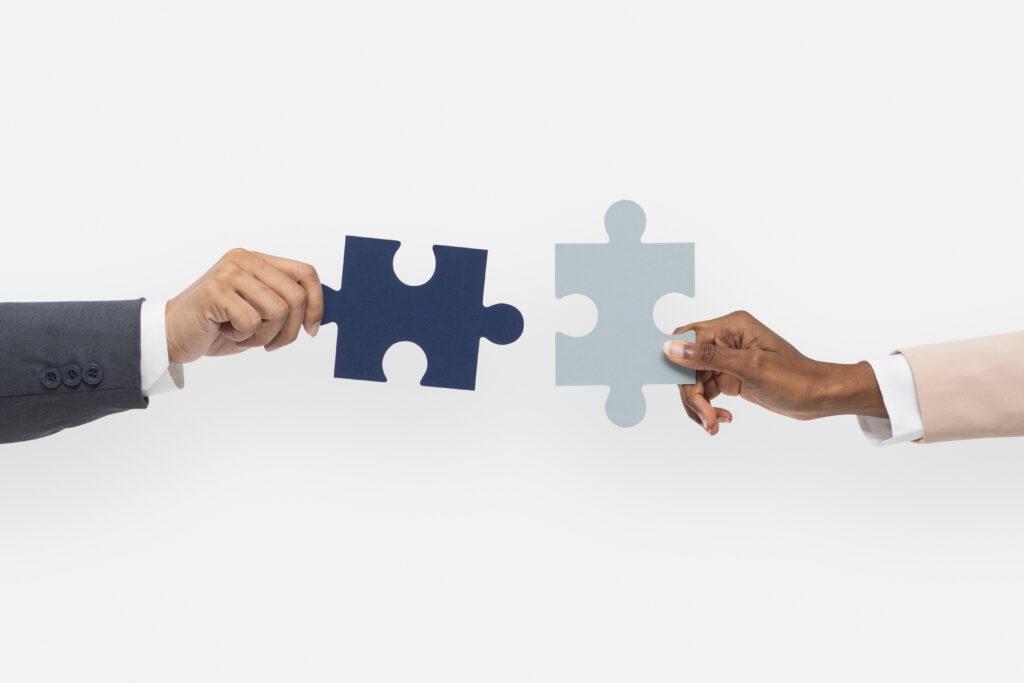 Two professionals holding puzzle pieces about to connect, representing collaboration in project management between teams or agencies and clients.